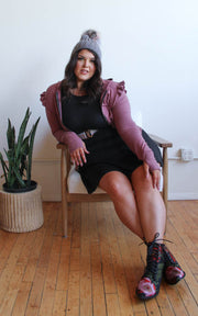 Plus size model sitting in chair wearing hoodie and minidress and hat with pom pom